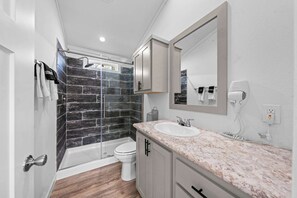 A modern bathroom with a glass-enclosed shower, a white toilet, a marble countertop, and a large mirror. - The Resort at Fredericksburg Unit 20 (Fredericksburg)