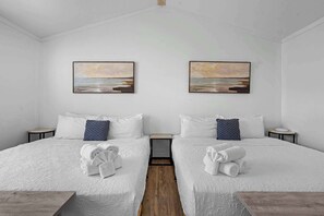 A double room with two beds, white bedding, and matching pillows. There are two paintings on the wall above the beds, and towels are neatly folded on the beds. - The Resort at Fredericksburg Unit 20 (Fredericksburg)
