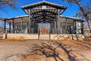 Un pavillon couvert, doté d’une base en pierre et d’une structure métallique, comprenant un escalier central et offrant une vue sur un cheval au loin.