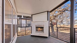 A covered outdoor deck with a stone fireplace, large windows, and a view of a tree-lined street. - The Resort at Fredericksburg Unit 25 (Fredericksburg)