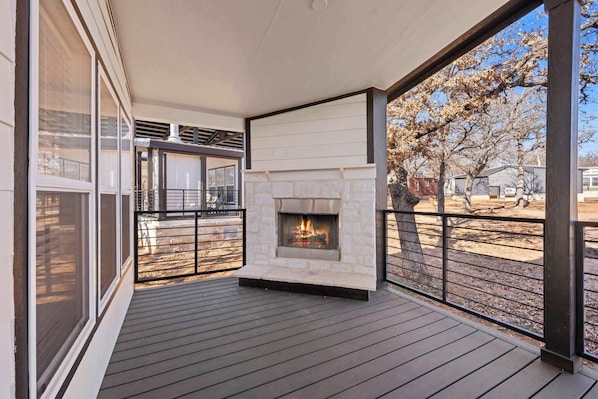 A covered outdoor deck with a stone fireplace, large windows, and a view of a tree-lined street. - The Resort at Fredericksburg Unit 25 (Fredericksburg)