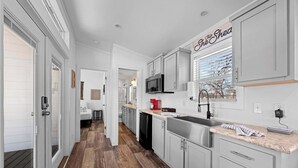 A modern kitchen with white cabinetry, a stainless steel sink, and a window with blinds. - The Resort at Fredericksburg Unit 25 (Fredericksburg)