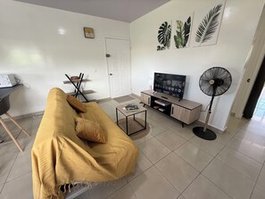Ein Wohnzimmer mit einer Couch, einem Fernseher, einem Ventilator und einer Tür.
