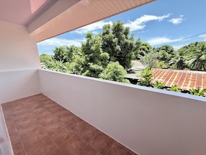 Ein Balkon mit Blick auf dichtes Grün und ein Ziegeldach.