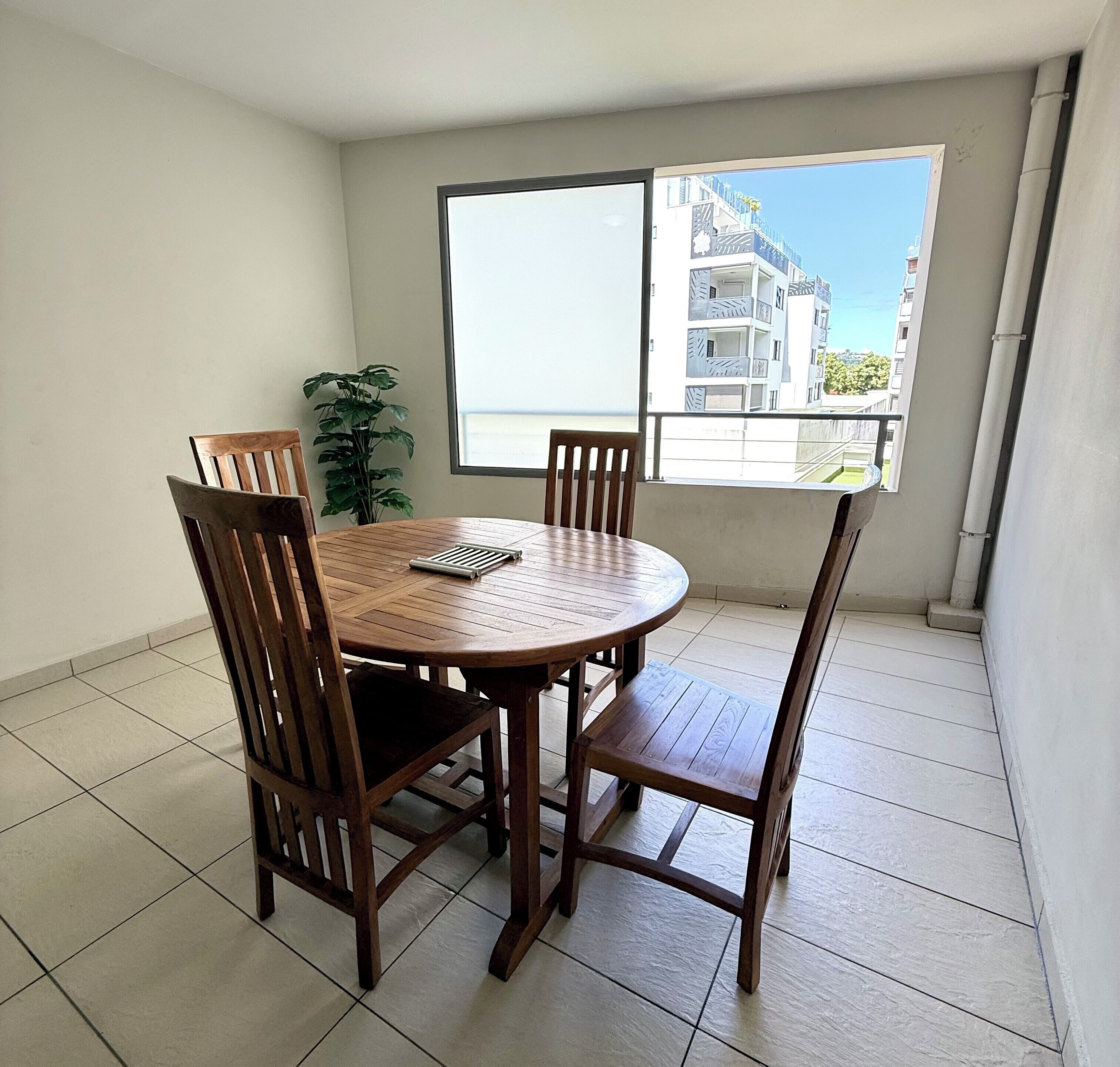 A dining area with a round wooden table and four chairs, a potted plant, and a large window with a view of buildings.
