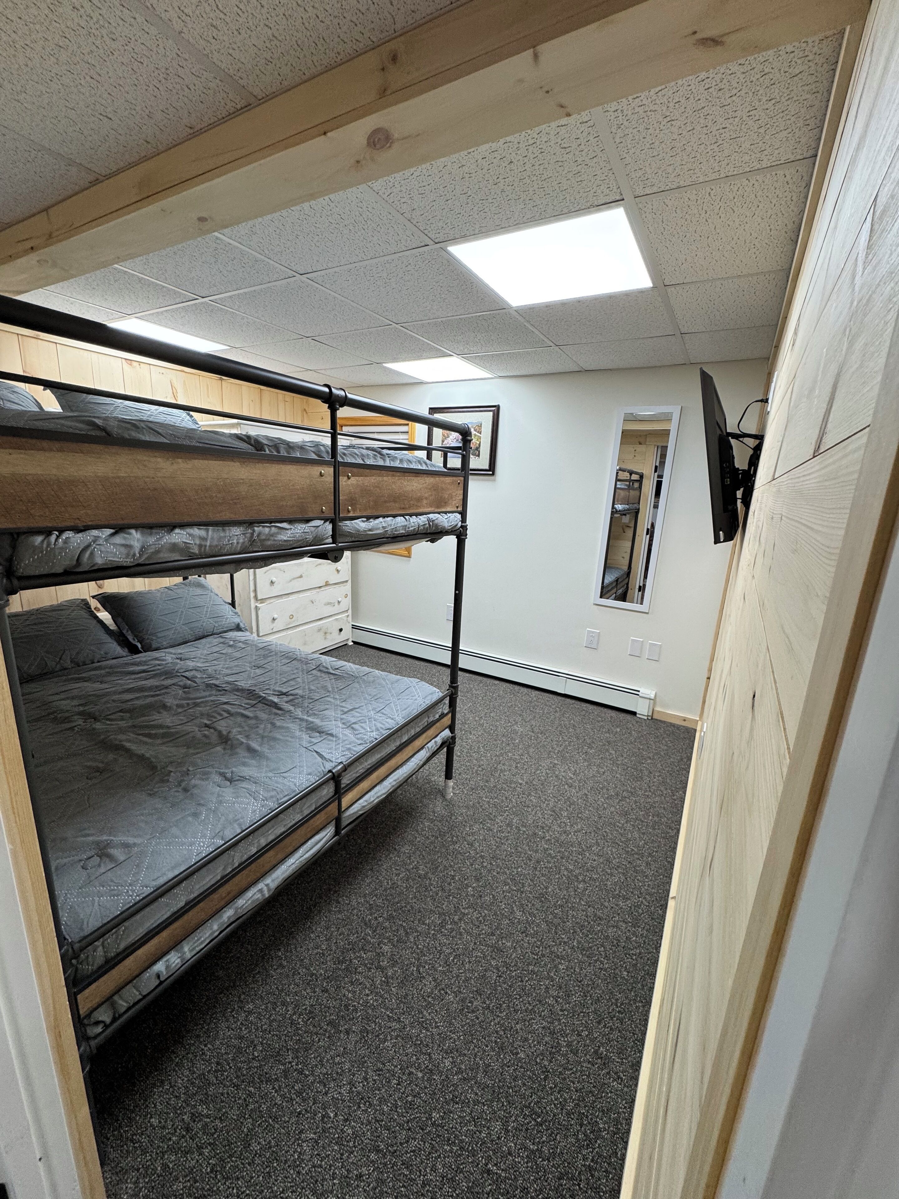 A bunk bed room with a wooden ceiling, a white wall, and a small window.