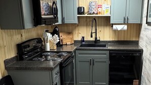 Una cocina compacta con gabinetes grises, una estufa negra y un lavavajillas.