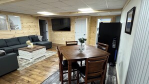 Un espacio de sala acogedor con piso de madera, un sofá, una mesa de comedor con sillas y un televisor de pantalla plana montado en la pared.