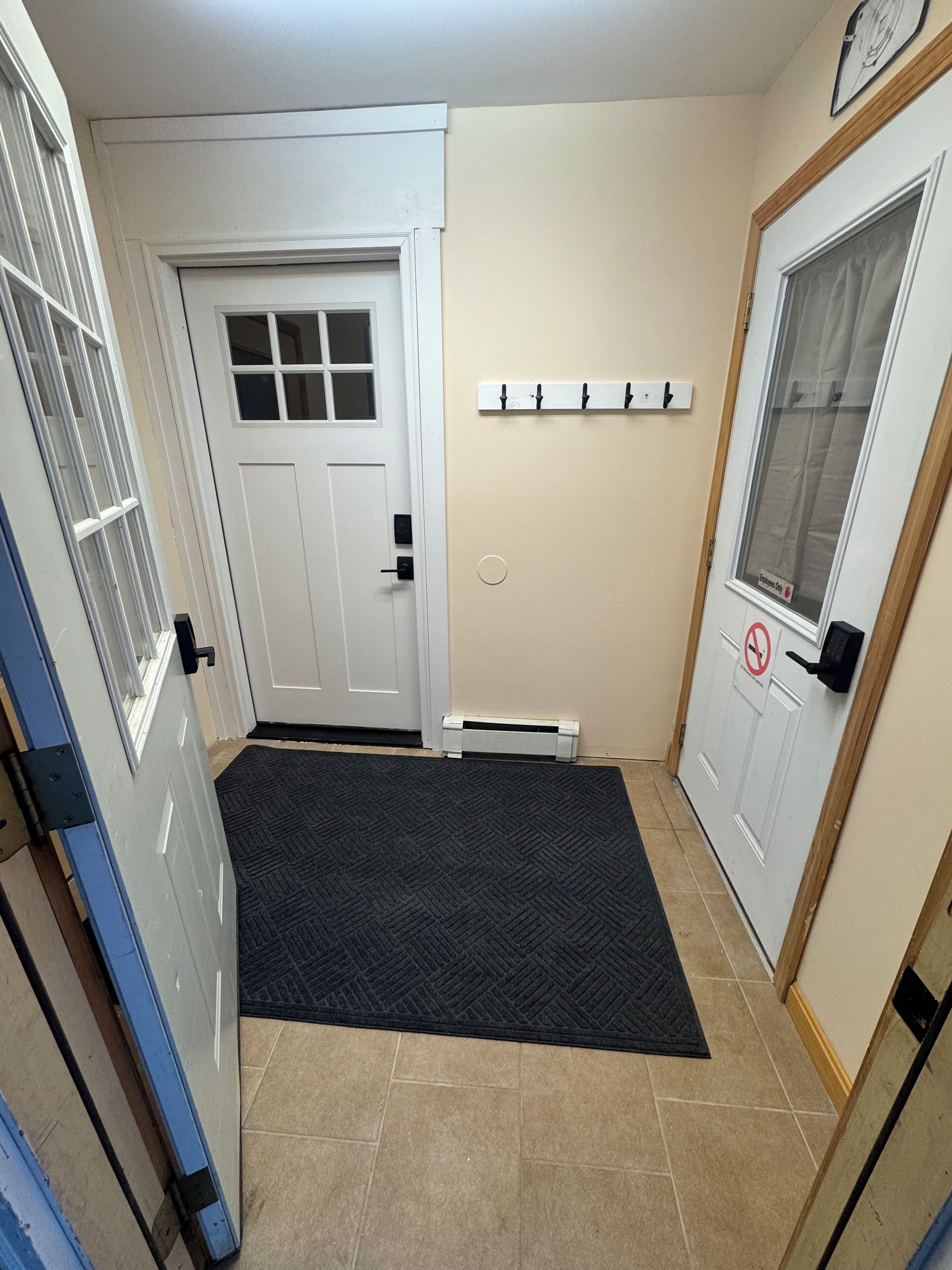 A hallway with a white door, a black mat at the entrance, a coat rack, and a no-smoking sign.