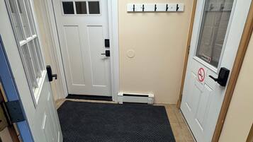 A hallway with a white door, a black mat at the entrance, a coat rack, and a no-smoking sign.