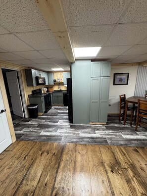 A kitchen with grey cabinets, a black refrigerator, and a wooden dining table with chairs.