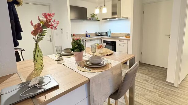 Eine moderne Küche mit weißen Schränken, einer Holzausziehtafel und einem Essbereich mit Stuhl und Tisch.