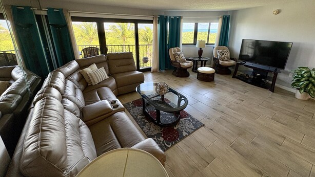 A living room with a leather sectional sofa, a glass coffee table, and a flat-screen TV. - Sunset, Large, Top Floor OceanFront Views, Island Condo - Key Largo (Key Largo)