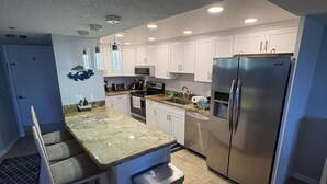 A modern kitchen with white cabinets, stainless steel appliances, and a granite countertop. - Sunset, Large, Top Floor OceanFront Views, Island Condo - Key Largo (Key Largo)
