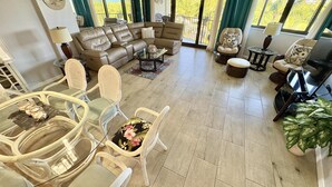 A spacious living area with a sectional sofa, wicker chairs, a dining table, and a TV. - Sunset, Large, Top Floor OceanFront Views, Island Condo - Key Largo (Key Largo)