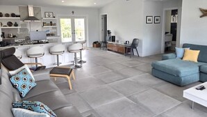 A modern living room with a grey sofa, a blue armchair, and a dining area with bar stools. - Sunset, Waterfront Key Largo House, with a 100' Boat Dock (Key Largo)