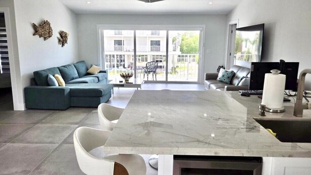 A modern kitchen with a marble countertop, white chairs, and a dining area. - Sunset, Waterfront Key Largo House, with a 100' Boat Dock (Key Largo)