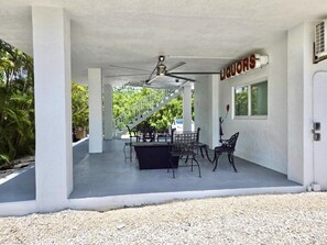 A covered outdoor area with a table and chairs, a ceiling fan, and a sign that reads "LIQUORS". - Sunset, Waterfront Key Largo House, with a 100' Boat Dock (Key Largo)