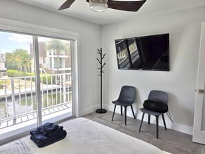 A modern hotel room with a large sliding glass door to a balcony, a flat-screen TV mounted on the wall, and two black chairs. - Sunset, Waterfront Key Largo House, with a 100' Boat Dock (Key Largo)