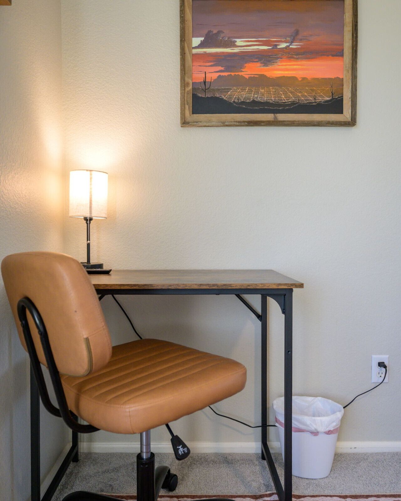 Un espace de travail comprenant un bureau, une chaise, une lampe et un tableau accroché au mur.