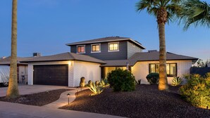 Ein zweistöckiges Haus mit Garage, Auffahrt und einem angelegten Garten mit Palmen und Sträuchern.