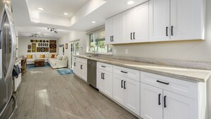 Eine moderne Küche mit weißen Schränken, einem Edelstahl-Kühlschrank und einem Essbereich mit einer weißen Couch und farbenfrohen Kissen.