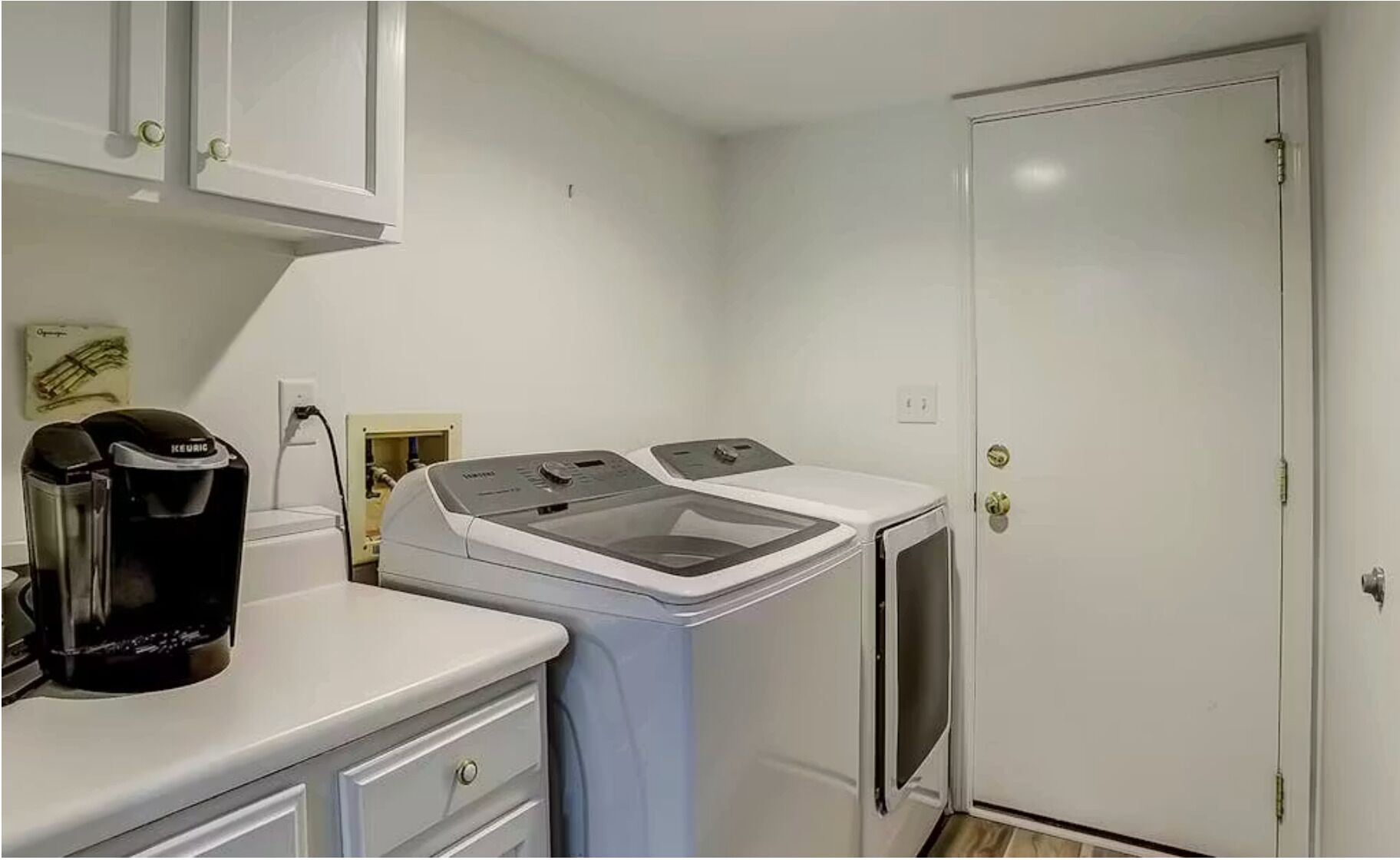 A compact laundry room with a front-loading washer and dryer, a coffee maker, and a cabinet above the counter.