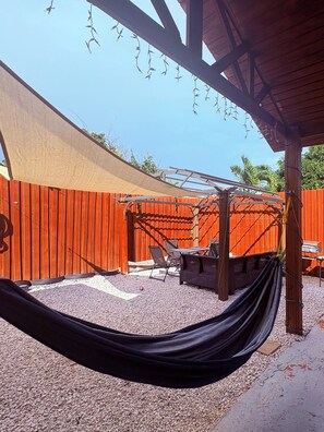 A covered outdoor seating area with a hammock, a grill, and a wooden fence. - Spacious Family Getaway in Guayama – Comfort Meets Convenience (Guayama)