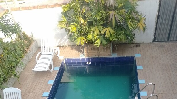 A rectangular swimming pool with a blue tiled edge, surrounded by a wooden deck. There are white lounge chairs and a green hose on the deck.