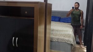 A room with a wardrobe, a bed with a patterned bedspread, and a mirror reflecting the room.