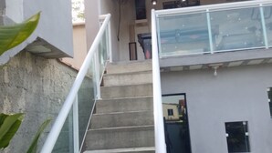 A staircase leading to a covered area with a glass railing, concrete steps, and a view of a building with a window and a door.