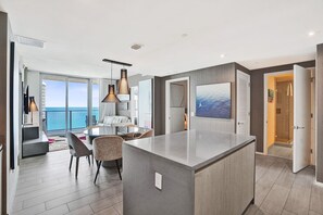 A modern hotel room with a large island in the center, a dining area with a view of the ocean, and a spacious living area with large windows. - 3BR Oceanview HYDE – Free Parking, No Resort Fees (Hollywood)