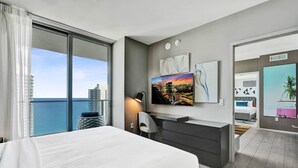 A modern hotel room with a large bed, a desk, a TV, and a view of the city and ocean. - 3BR Oceanview HYDE – Free Parking, No Resort Fees (Hollywood)