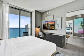 A modern hotel room with a large bed, a desk, a TV, and a view of the city and ocean. - 3BR Oceanview HYDE – Free Parking, No Resort Fees (Hollywood)