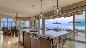 Een moderne keuken met een groot kookeiland, roestvrijstalen apparatuur en grote ramen met uitzicht op de oceaan.