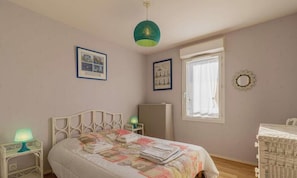 Ein Schlafzimmer mit einem Bett, zwei Nachttischen, einer Lampe, einer Kommode, einem Fenster und einer Wanddekoration.