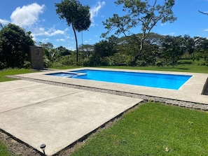 A rectangular swimming pool with a concrete deck, surrounded by grass and trees.