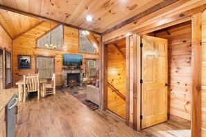 A log cabin interior with a fireplace, wooden walls, a dining area, and a large door. - Quiet 3BR - Near downtown - HotTub Arcade Theater (Gatlinburg)