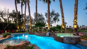 Une piscine avec un jacuzzi, entourée de palmiers et d’un jardin aménagé.