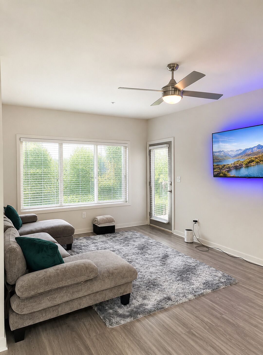 A living room with a sofa, a ceiling fan, a TV, and large windows.