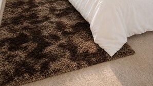 Een slaapkamer met een bed, een raam met jaloezieën, een spiegel en een vloerkleed.