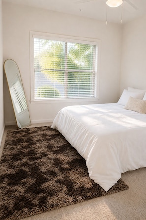 Une chambre à coucher avec un lit, une fenêtre avec des stores, un miroir et une moquette.
