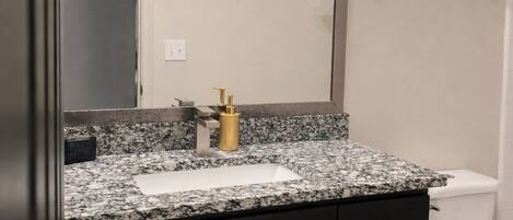 A bathroom with a granite countertop, a white sink, a gold faucet, a black cabinet with silver handles, a white toilet, and a wall-mounted towel rack.