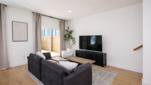 A modern living room with a grey sectional sofa, a wooden coffee table, a flat-screen TV on a black stand, and a potted plant. - NEW MODERN 1500 SQ FT RETREAT, 65” TV, Fire Pit, Family & Pet Friendly, Sleeps 6 (Boiling Springs)
