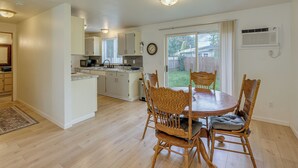 A spacious kitchen with white cabinets, a dining area with a wooden table and chairs, and a large window with a view of the backyard. - Dog-Friendly Townhome Near Stillaguamish River! (Arlington)