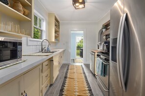 Eine schmale Küche mit Mikrowelle, Spüle und Edelstahl-Kühlschrank.