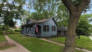 Ein zweistöckiges Haus mit Veranda, Flagge und einem großen Baum davor.
