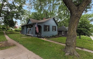 Ein zweistöckiges Haus mit Veranda, Flagge und einem großen Baum davor.