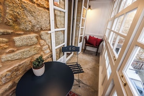 A stone wall, a black table with a potted plant, a red pillow on a chair, and a window with a view of the outside.