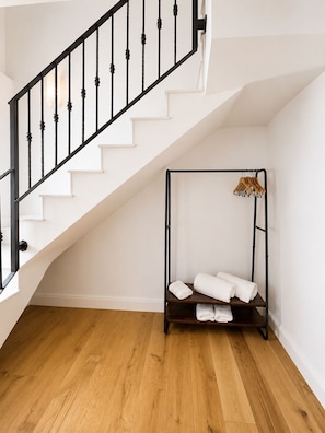 A staircase with black railings, a wooden floor, and a corner with a metal bed frame and white towels. - Do Bico Rooms (Camariñas)